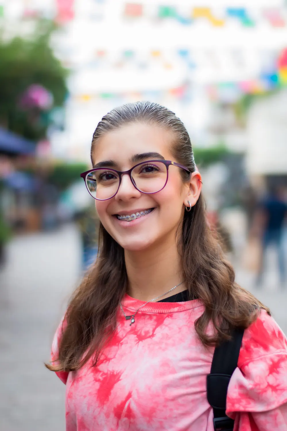 A teenage girl with glasses and fixed braces smiling in a sunlit street