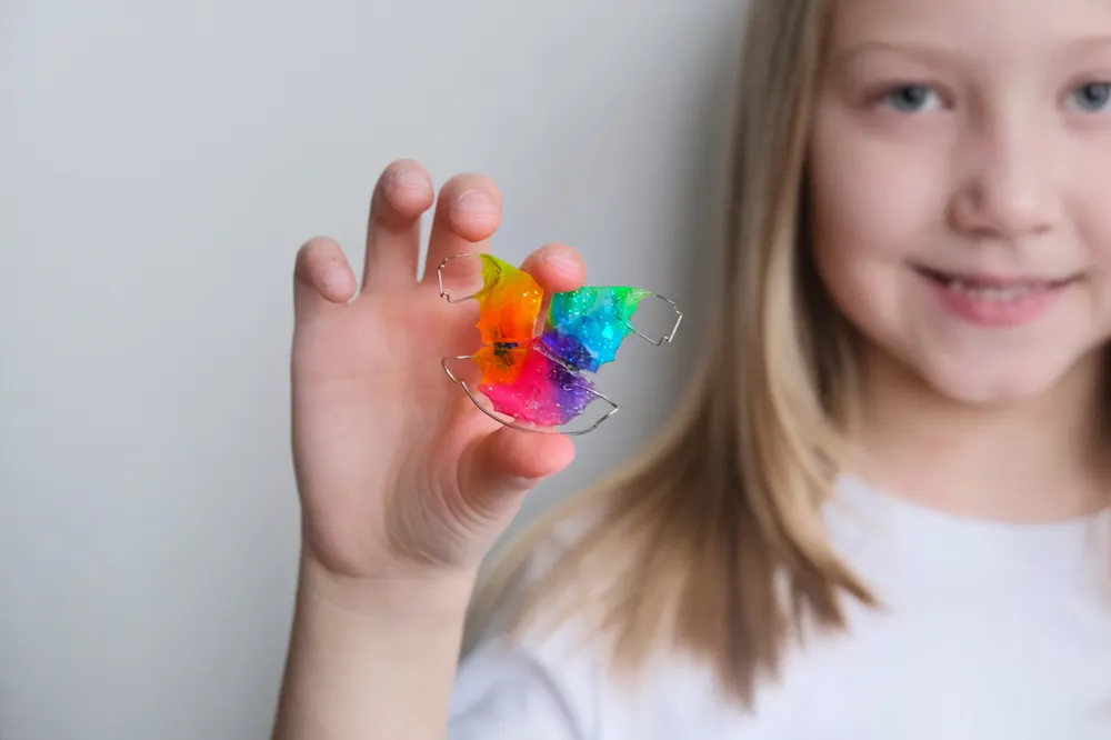 A child holding up a removable brace with a brightly coloured acrylic plate