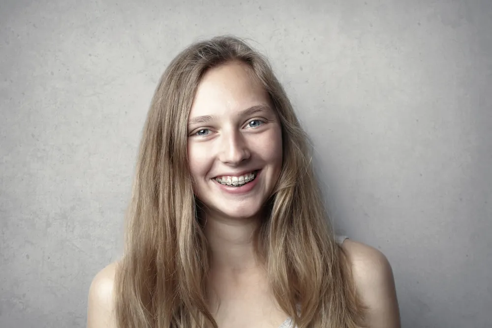 A teenage girl with fixed braces smiling in front of a pale wall